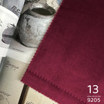 Close-up of a burgundy fabric with a textured surface, placed on top of books and a metallic container.
