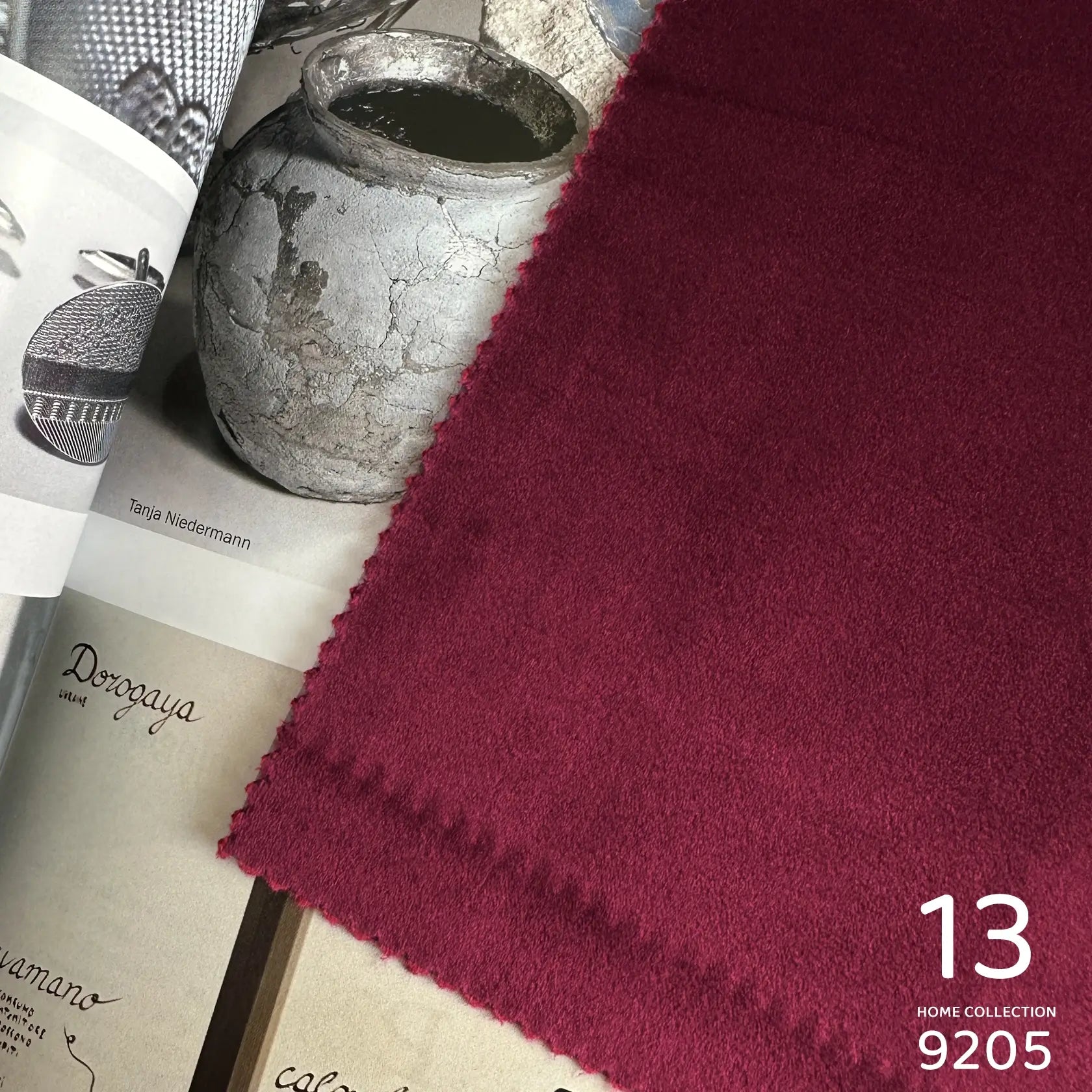 Close-up of a burgundy fabric with a textured surface, placed on top of books and a metallic container.
