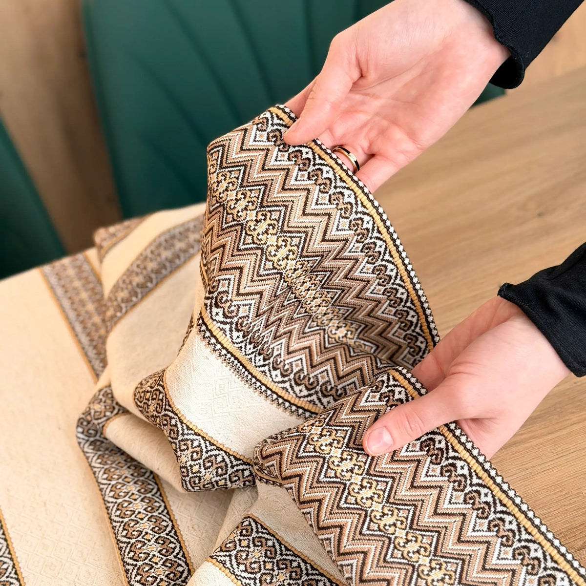 Close-up of a person holding a decorative fabric with intricate patterns on a wooden surface.