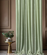 Green curtain with a subtle pattern in a room with a gold side table and plant.
