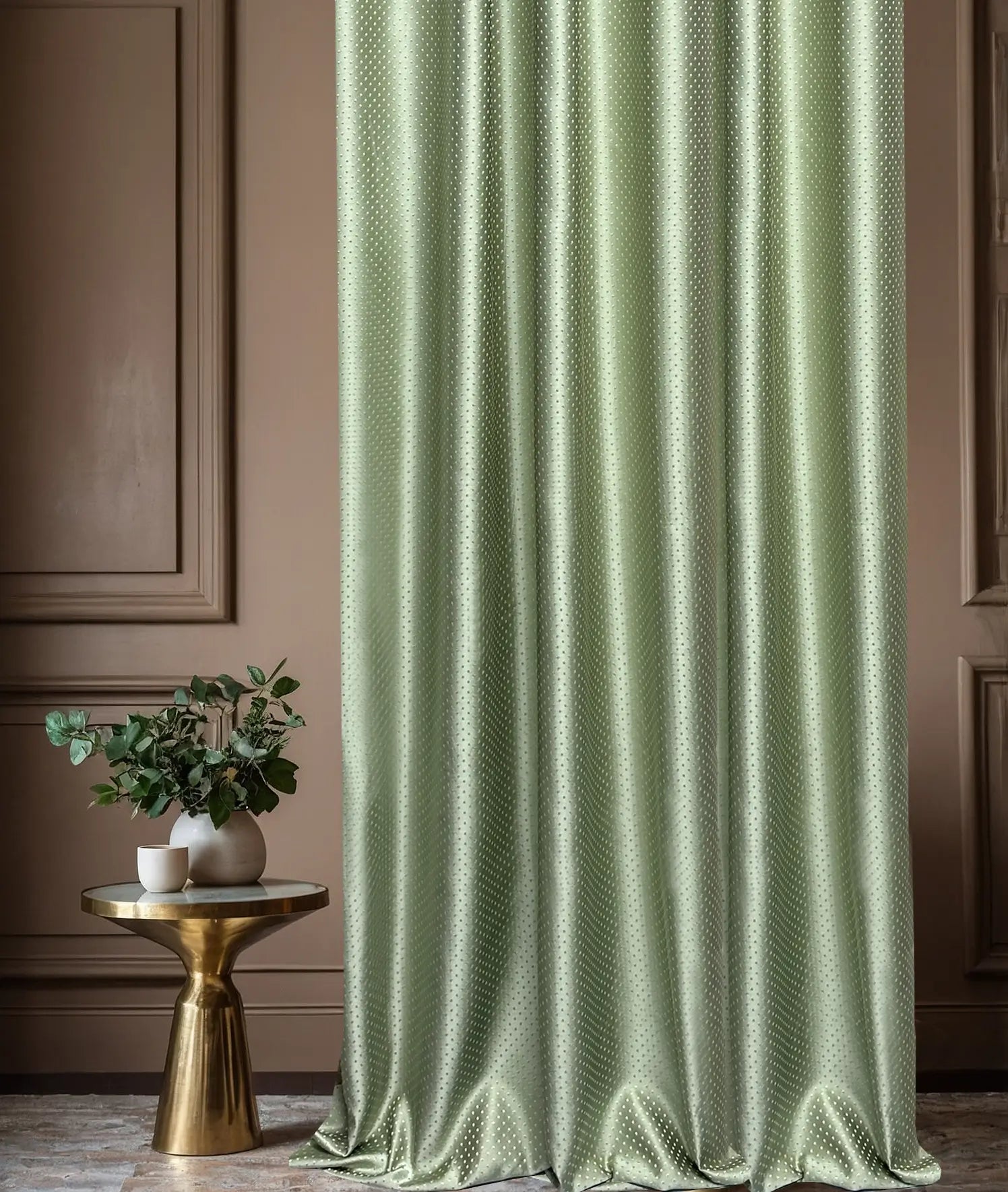 Green curtain with a subtle pattern in a room with a gold side table and plant.
