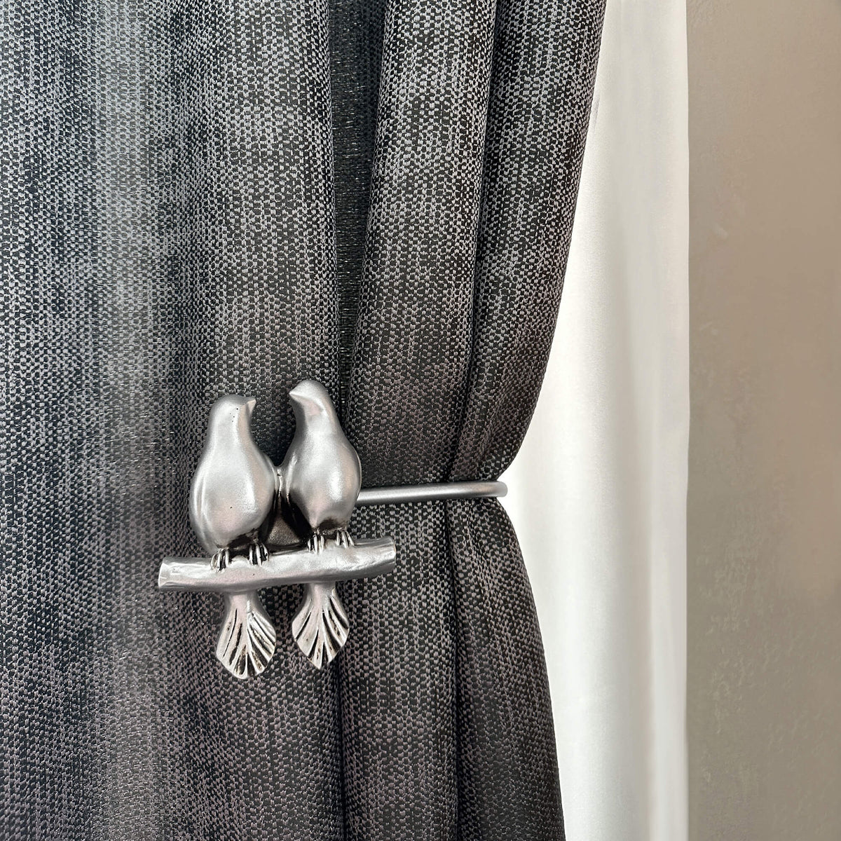 Decorative curtain tieback with bird design on a gray curtain.
