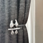 Decorative curtain tieback with bird design on a gray curtain.