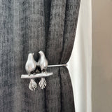 Decorative curtain tieback with bird design on a gray curtain.