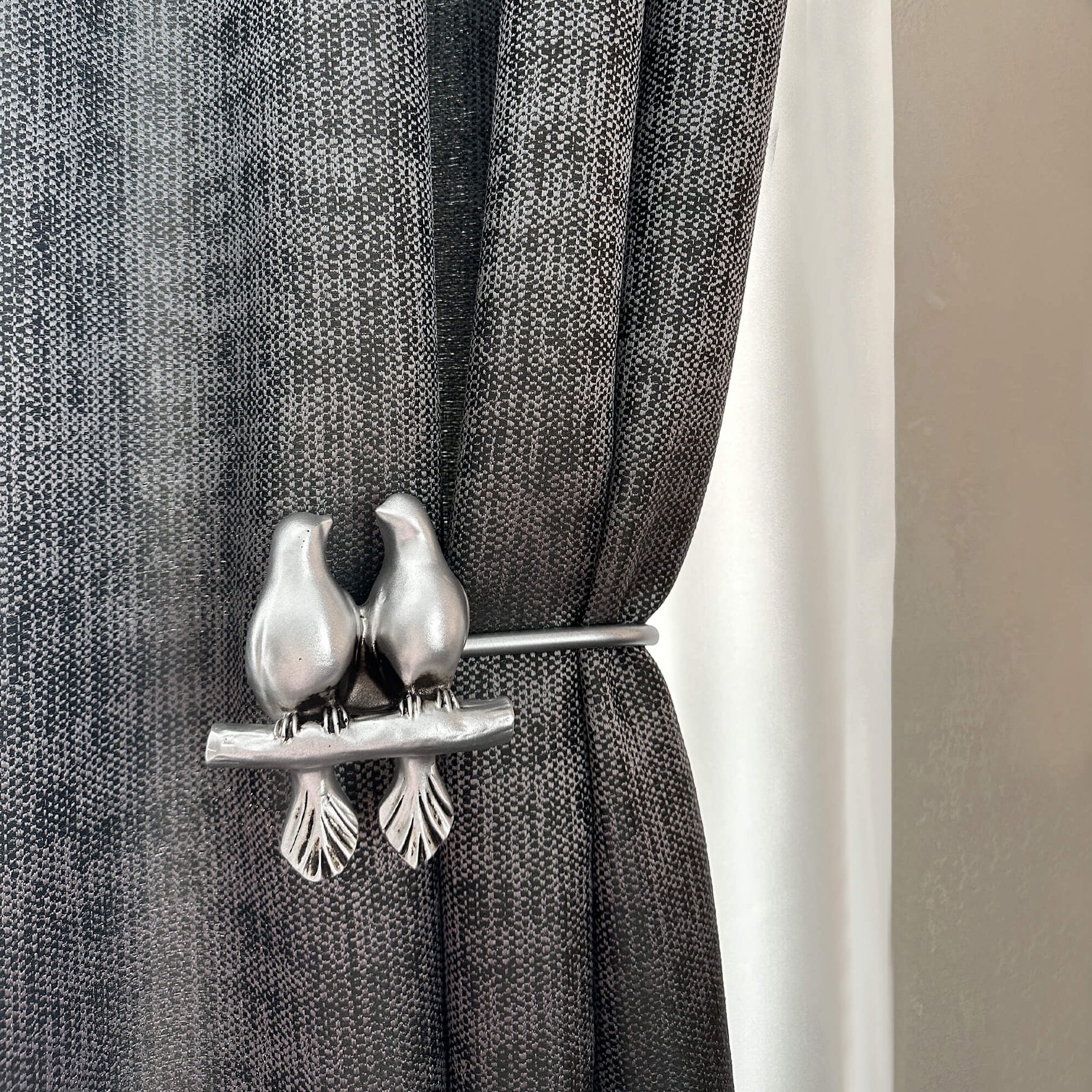 Decorative curtain tieback with bird design on a gray curtain.
