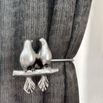 Decorative curtain tieback with bird design on a gray curtain.