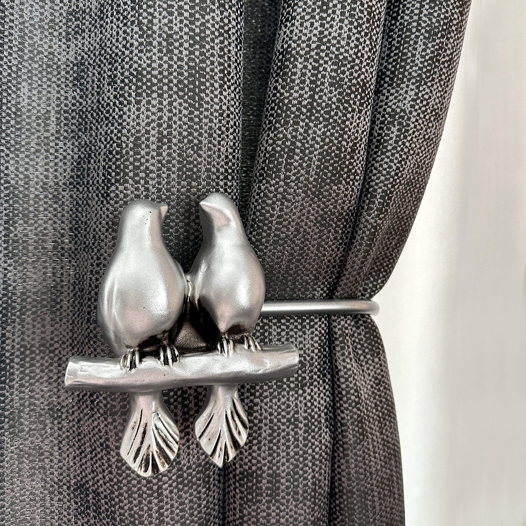 Decorative curtain tieback with bird design on a gray curtain.