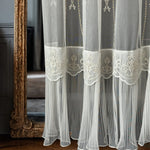 White embroidered curtain with ruffled skirt in front of a decorative mirror