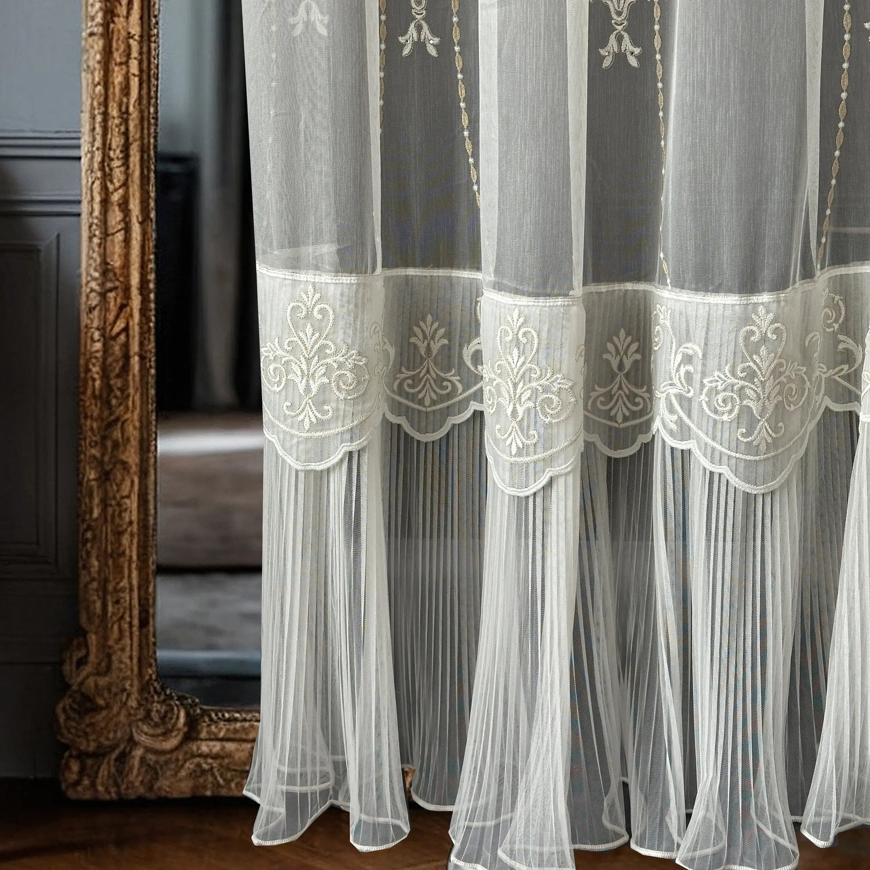 White embroidered curtain with ruffled skirt in front of a decorative mirror
