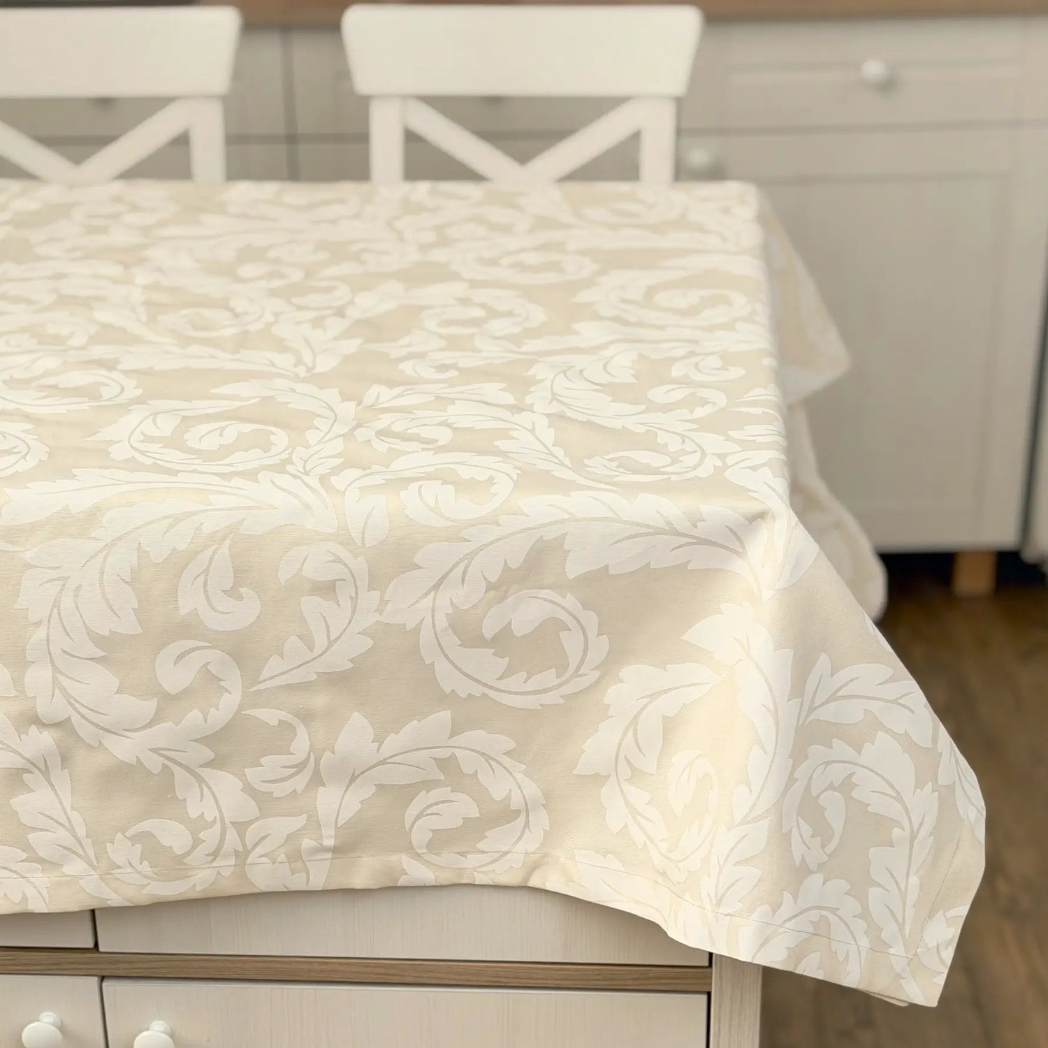 Beige patterned tablecloth on a dining table with white chairs in a kitchen setting.