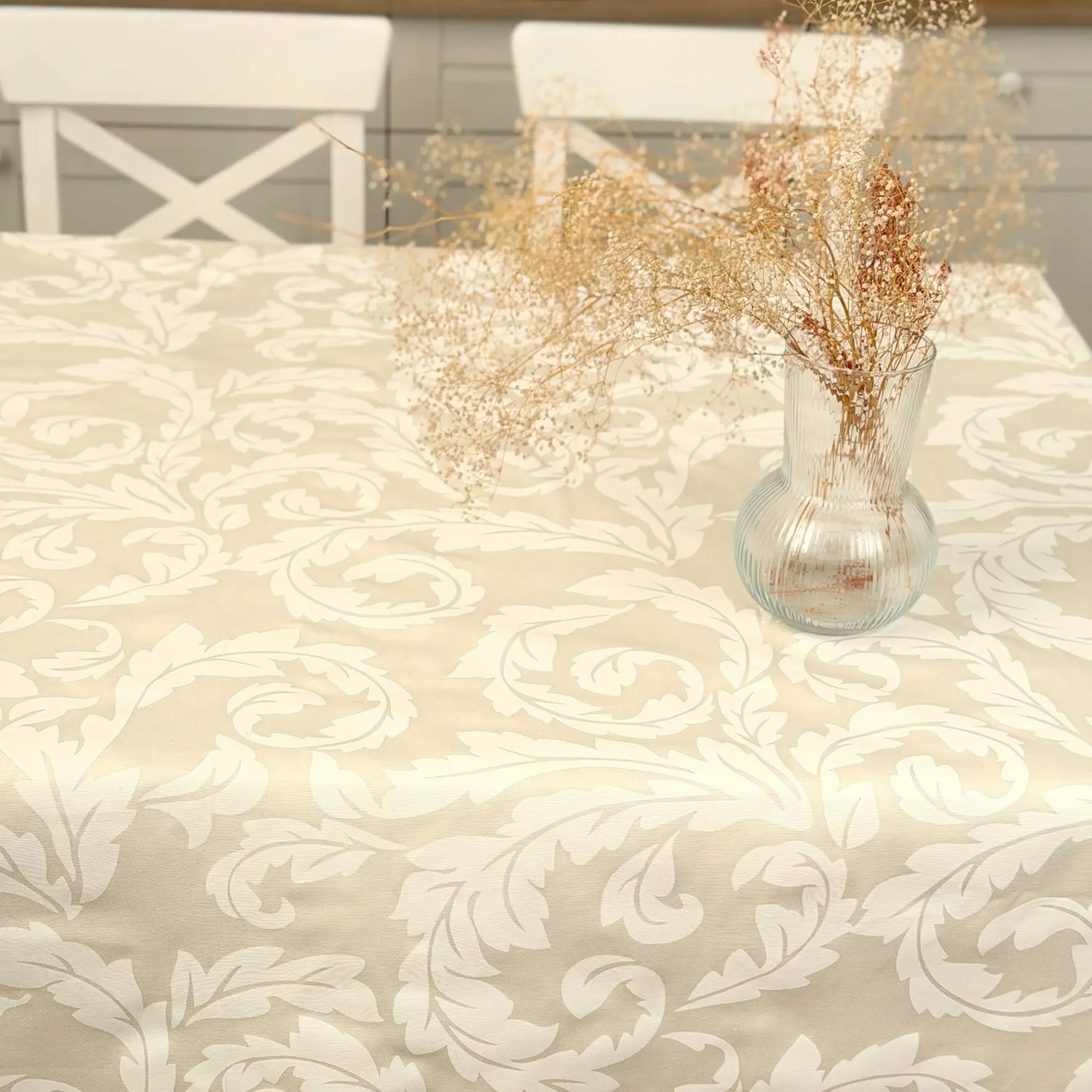 Decorative tablecloth with intricate patterns and a vase with dried flowers on a table.