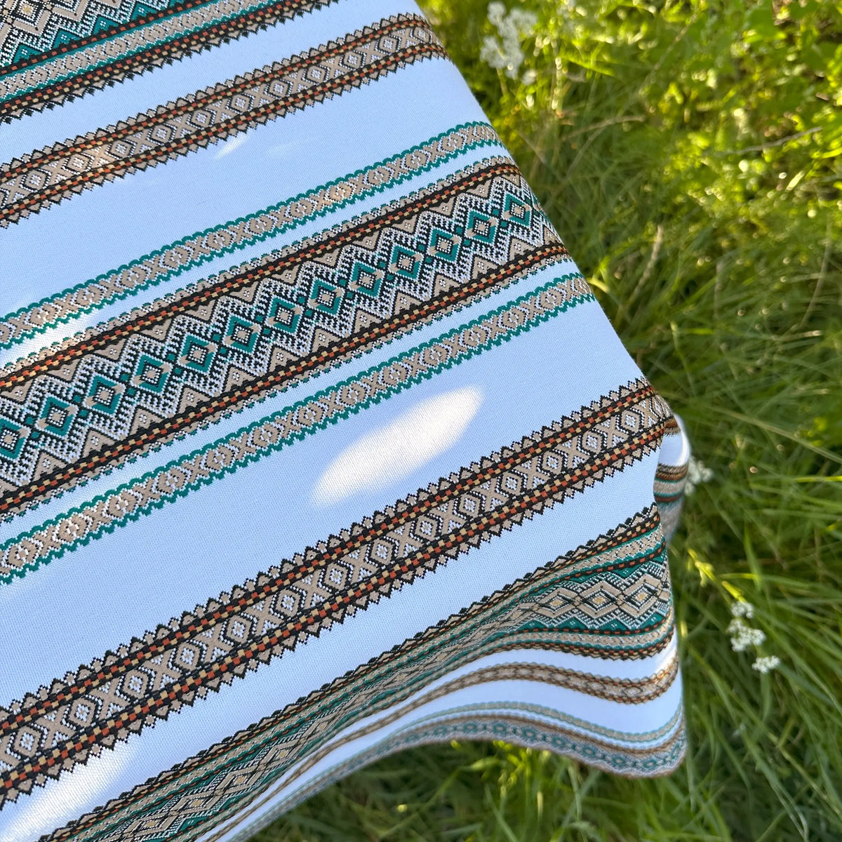 Close-up of a patterned fabric with stripes and geometric designs on grass.