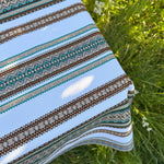 Close-up of a patterned fabric with stripes and geometric designs on grass.