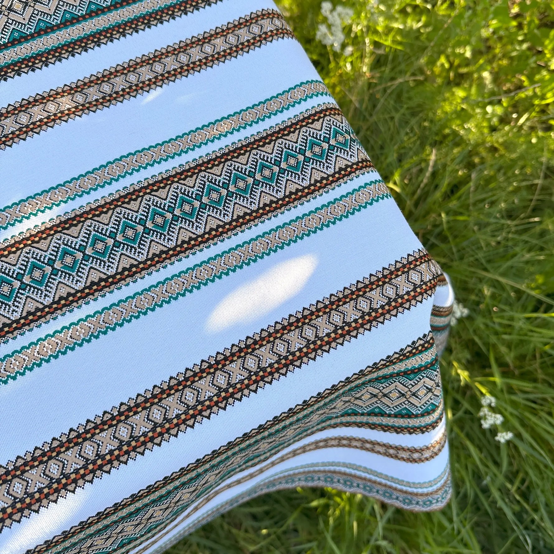 Close-up of a patterned fabric with stripes and geometric designs on grass.