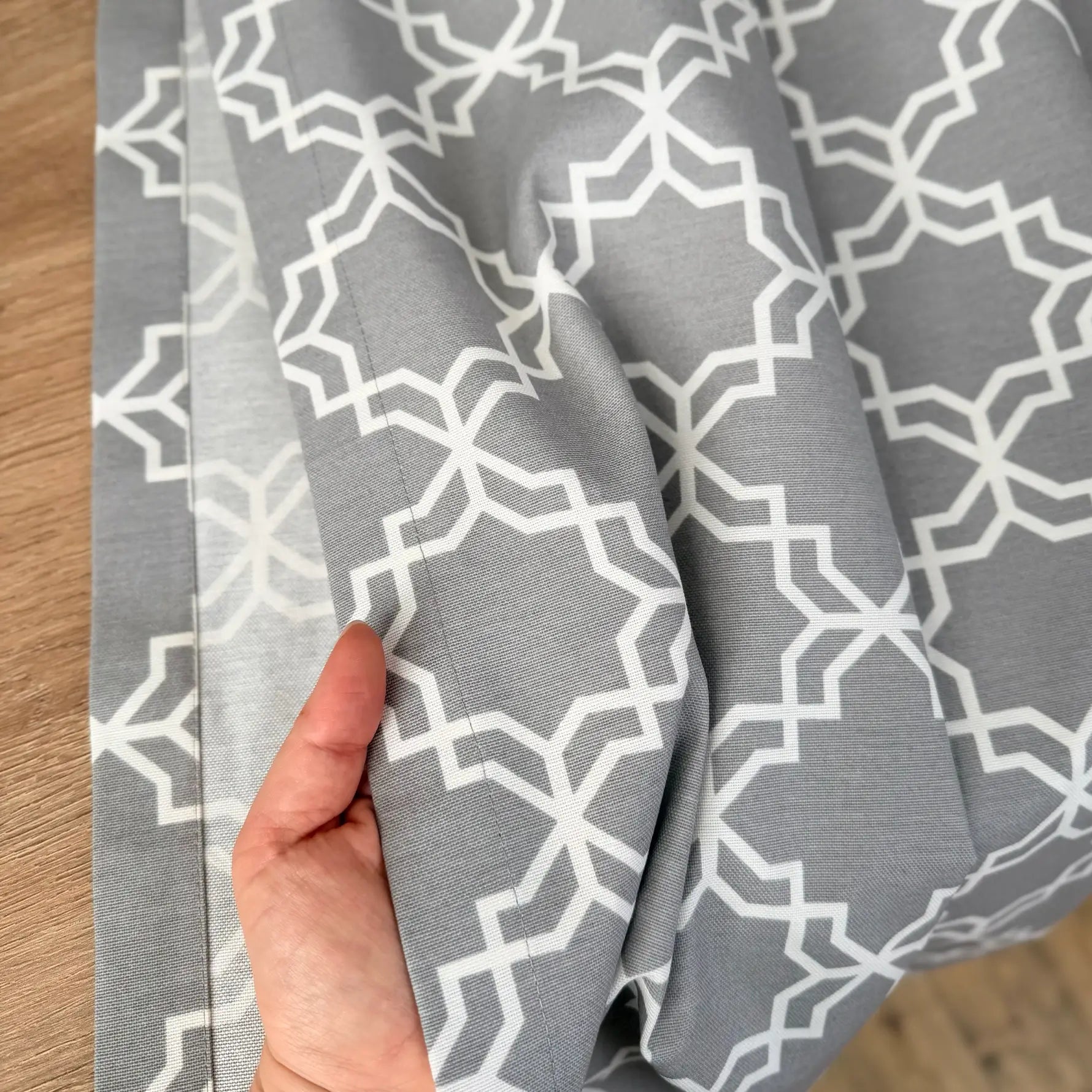 Gray fabric with white geometric pattern held by a hand on a wooden surface
