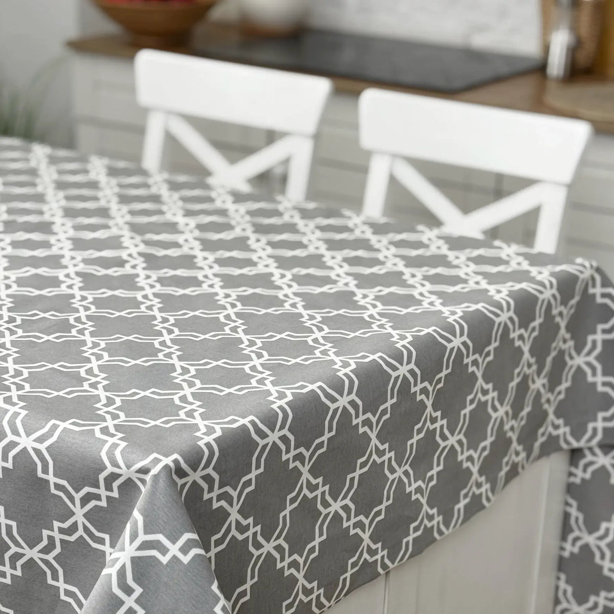 Gray geometric patterned tablecloth on a dining table with white chairs.