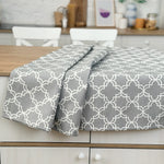Gray and white patterned tablecloth on a wooden table with a kitchen background