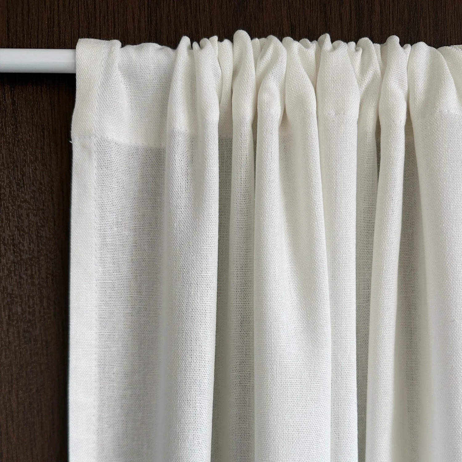 Close-up of a white curtain with a wooden rod on a dark background