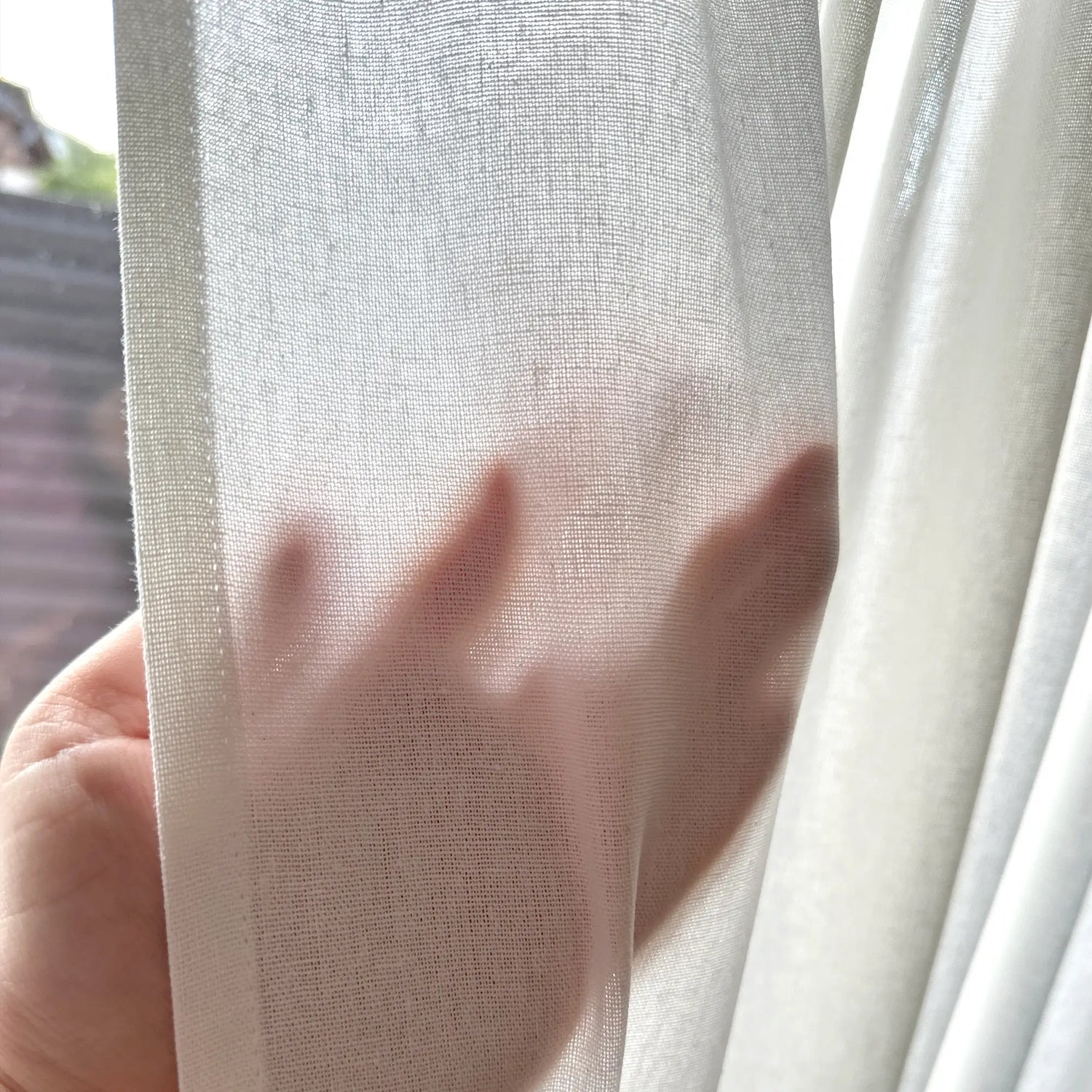 Close-up of a hand holding a sheer white curtain
