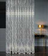 Decorative lace curtain in a room with a lamp and table.
