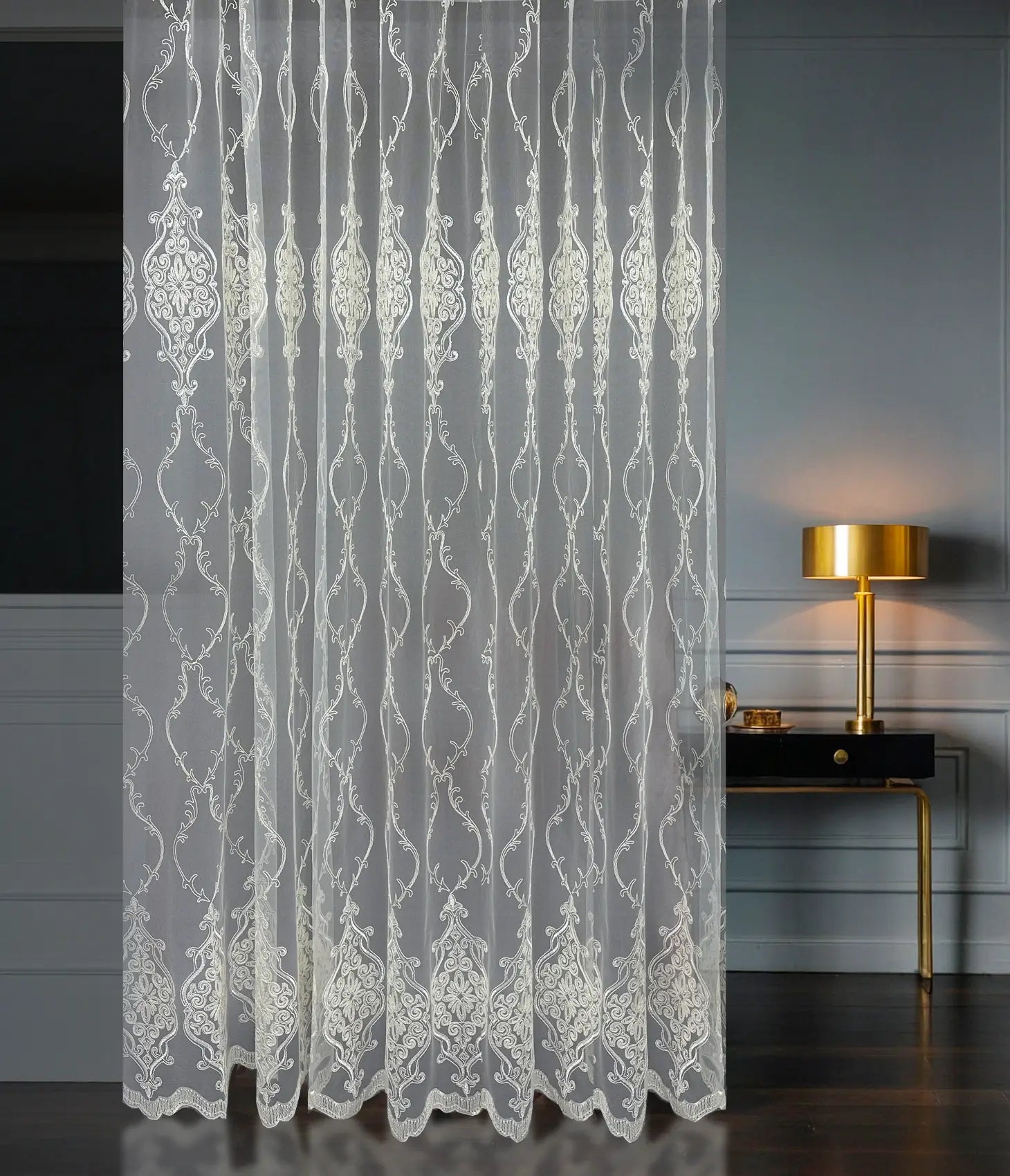 Decorative lace curtain in a room with a lamp and table.