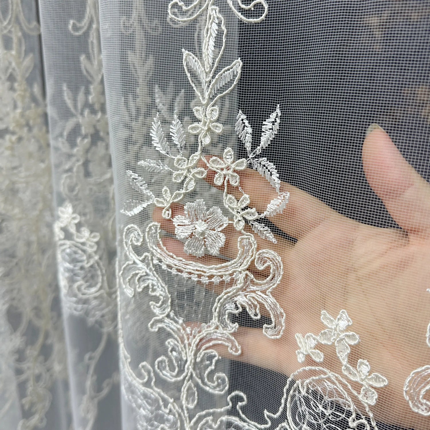 Close-up of lace fabric with floral embroidery held by a hand.