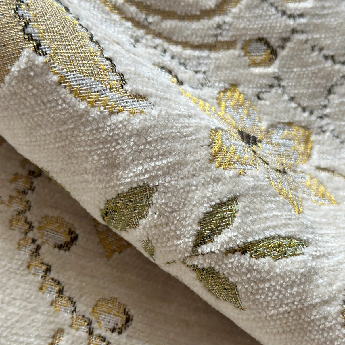 Close-up of embroidered fabric with gold and black patterns on a beige background