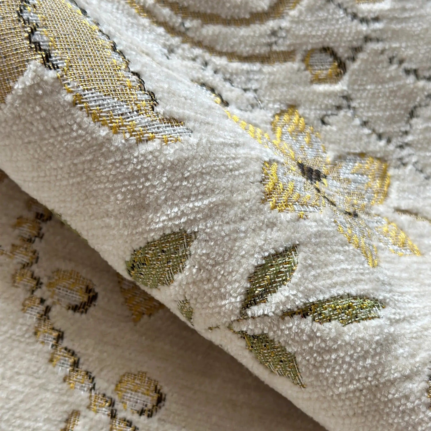Close-up of embroidered fabric with gold and black patterns on a beige background
