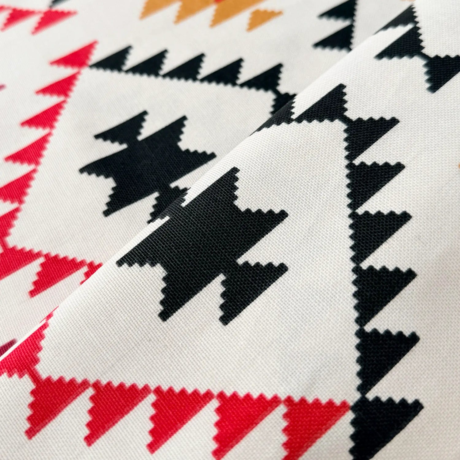 Close-up of fabric with geometric pattern featuring black, red, and orange triangles on a white background.