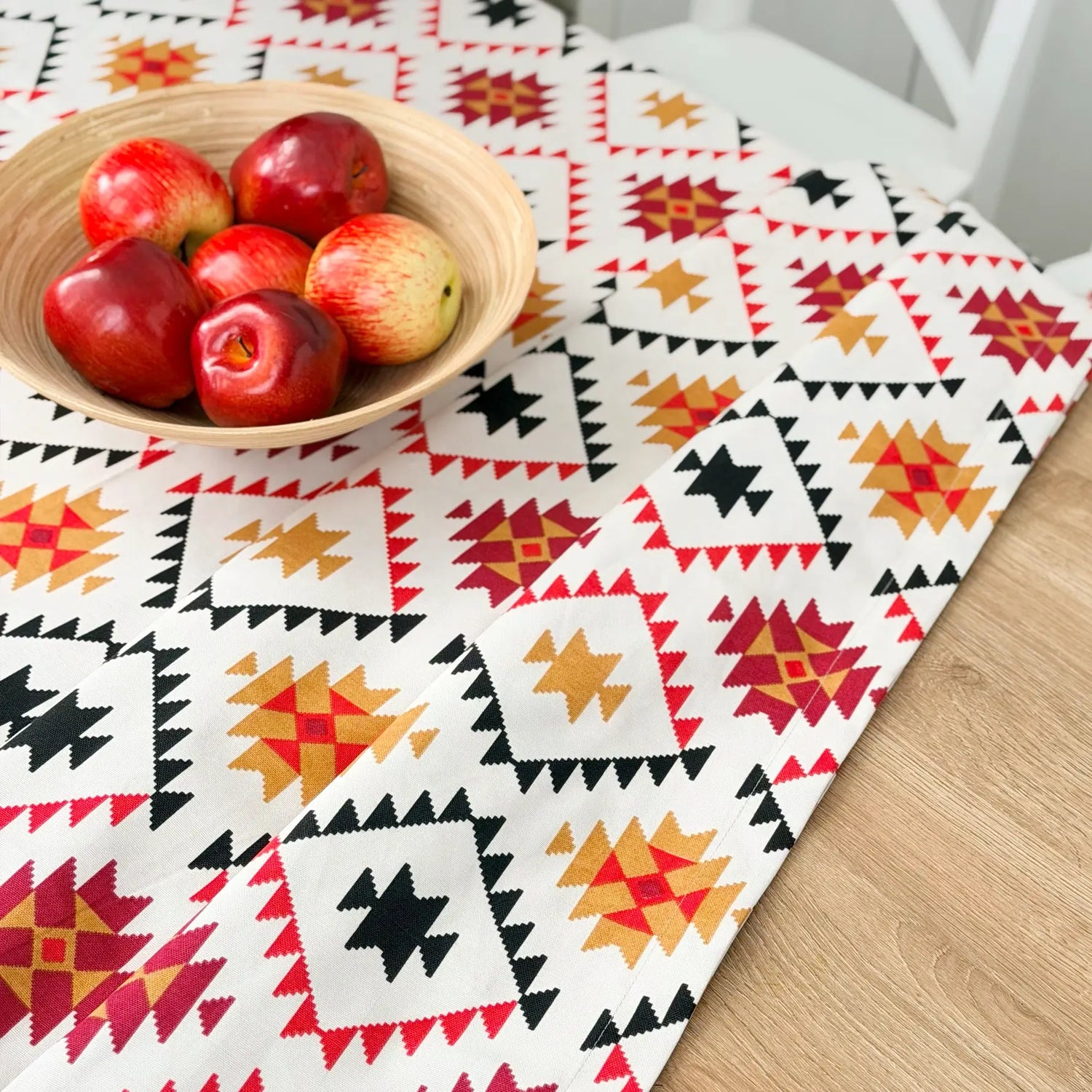 Colorful geometric-patterned tablecloth with a bowl of apples on a wooden table.