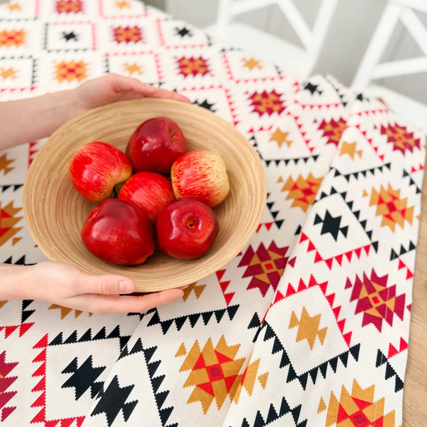 Person holding a bowl of red apples on a patterned tablecloth
