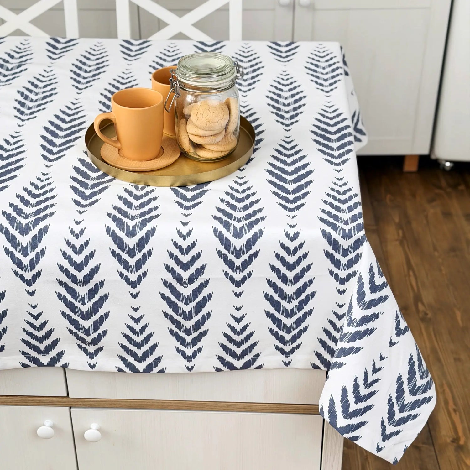 Tablecloth with blue leaf pattern on a table with a cup and cookies.