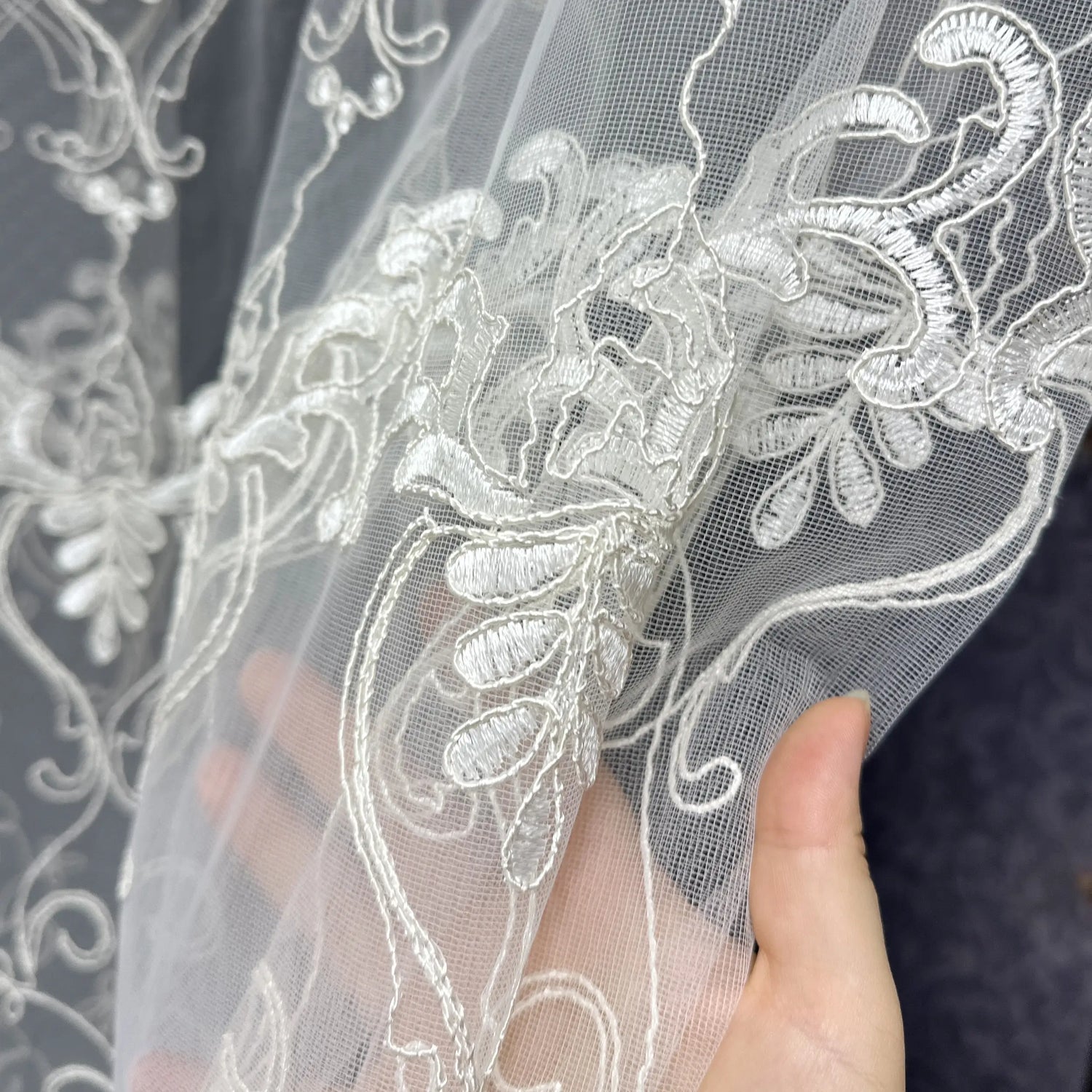 Close-up of a lace fabric with intricate designs held by a hand against a dark background.