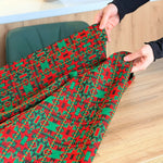 Red and green patterned fabric being held by hands on a wooden surface
