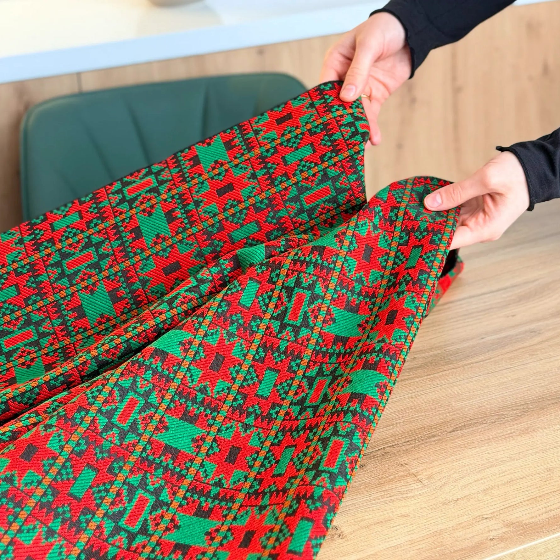 Red and green patterned fabric being held by hands on a wooden surface