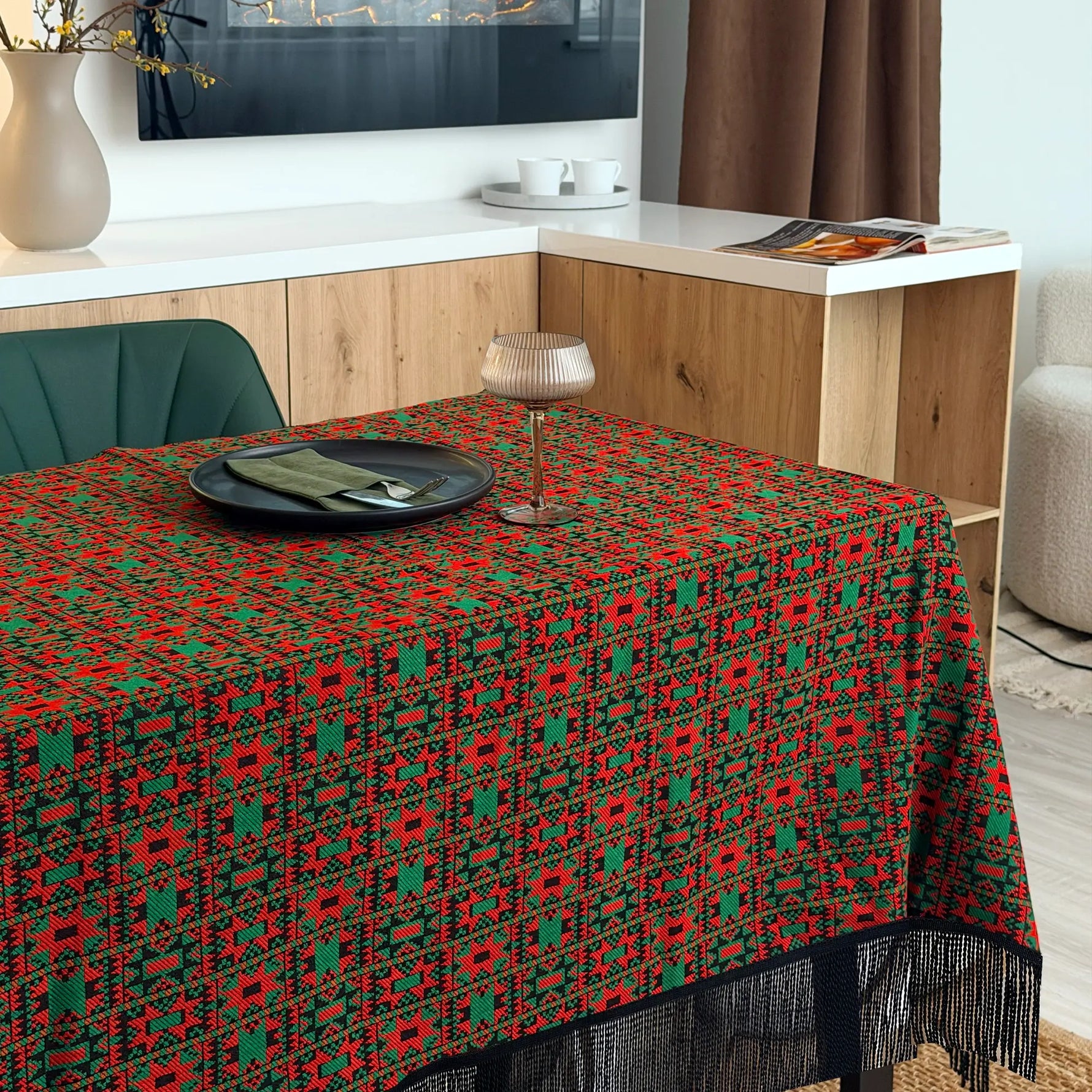 Dining table with a red and green patterned tablecloth in a modern kitchen setting.