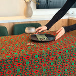 Person setting a table with a red and green patterned tablecloth.