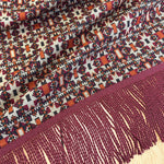 Close-up of a patterned fabric with fringes on a wooden surface