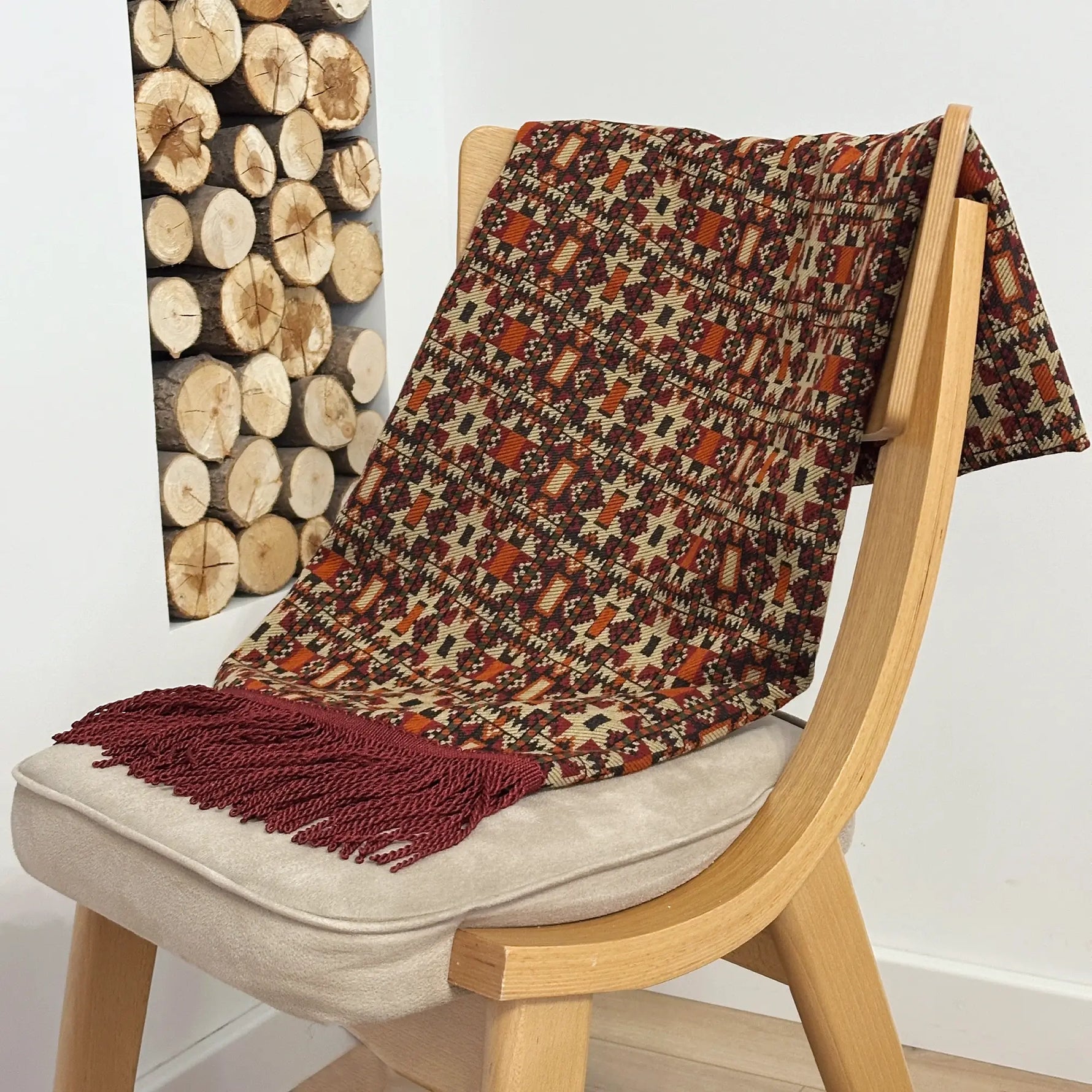 Patterned blanket draped over a wooden chair with a wooden log wall in the background