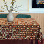 Table with a patterned tablecloth, vase with branches, and blurred background
