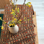 Patterned tablecloth with a vase of yellow flowers on a wooden surface