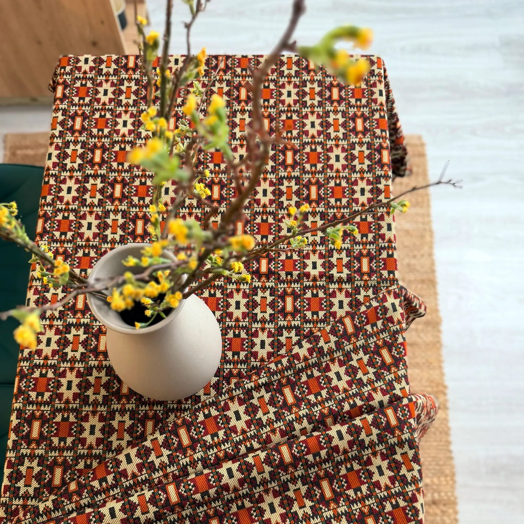 Patterned tablecloth with a vase of yellow flowers on a wooden surface