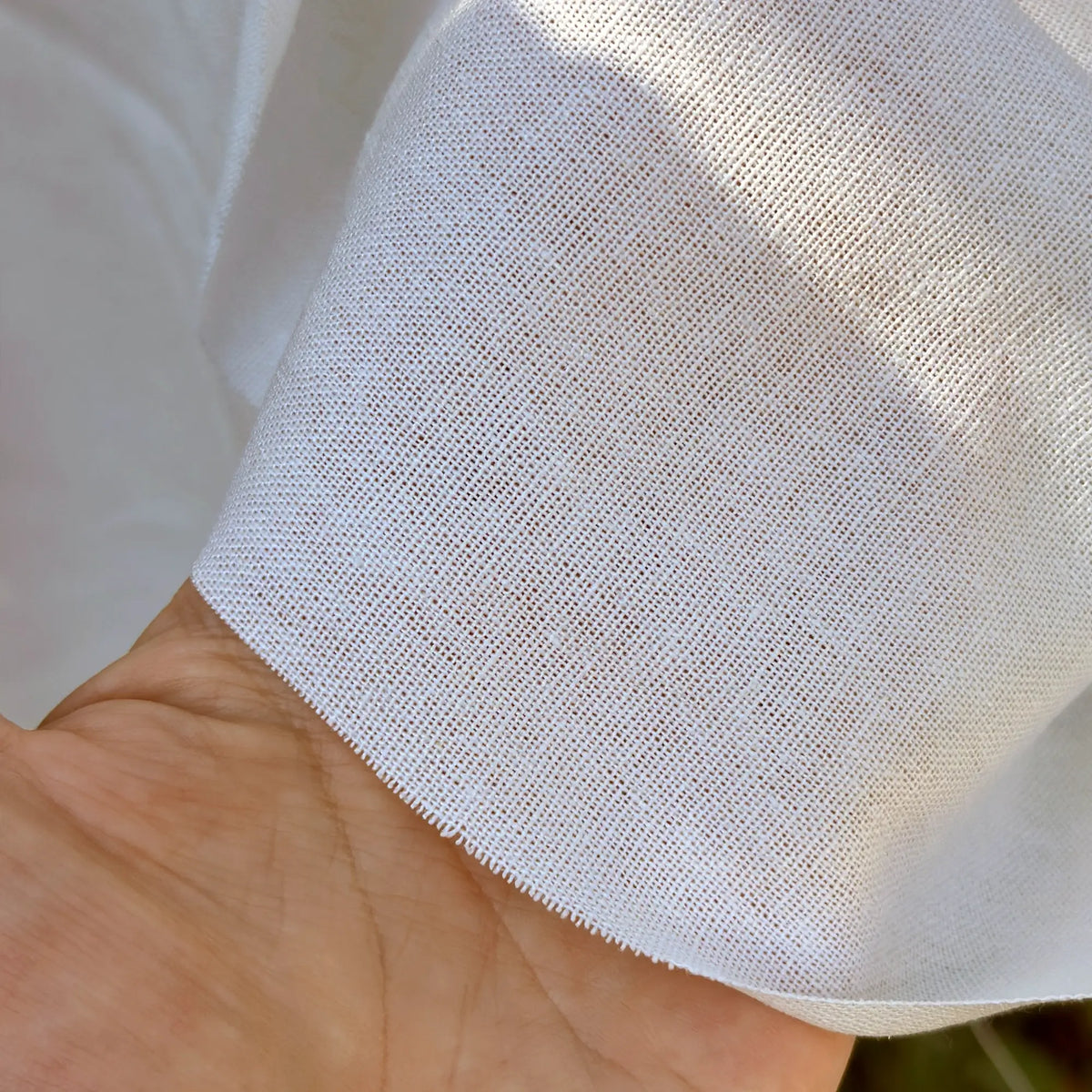 Close-up of a hand holding white fabric with a textured pattern.