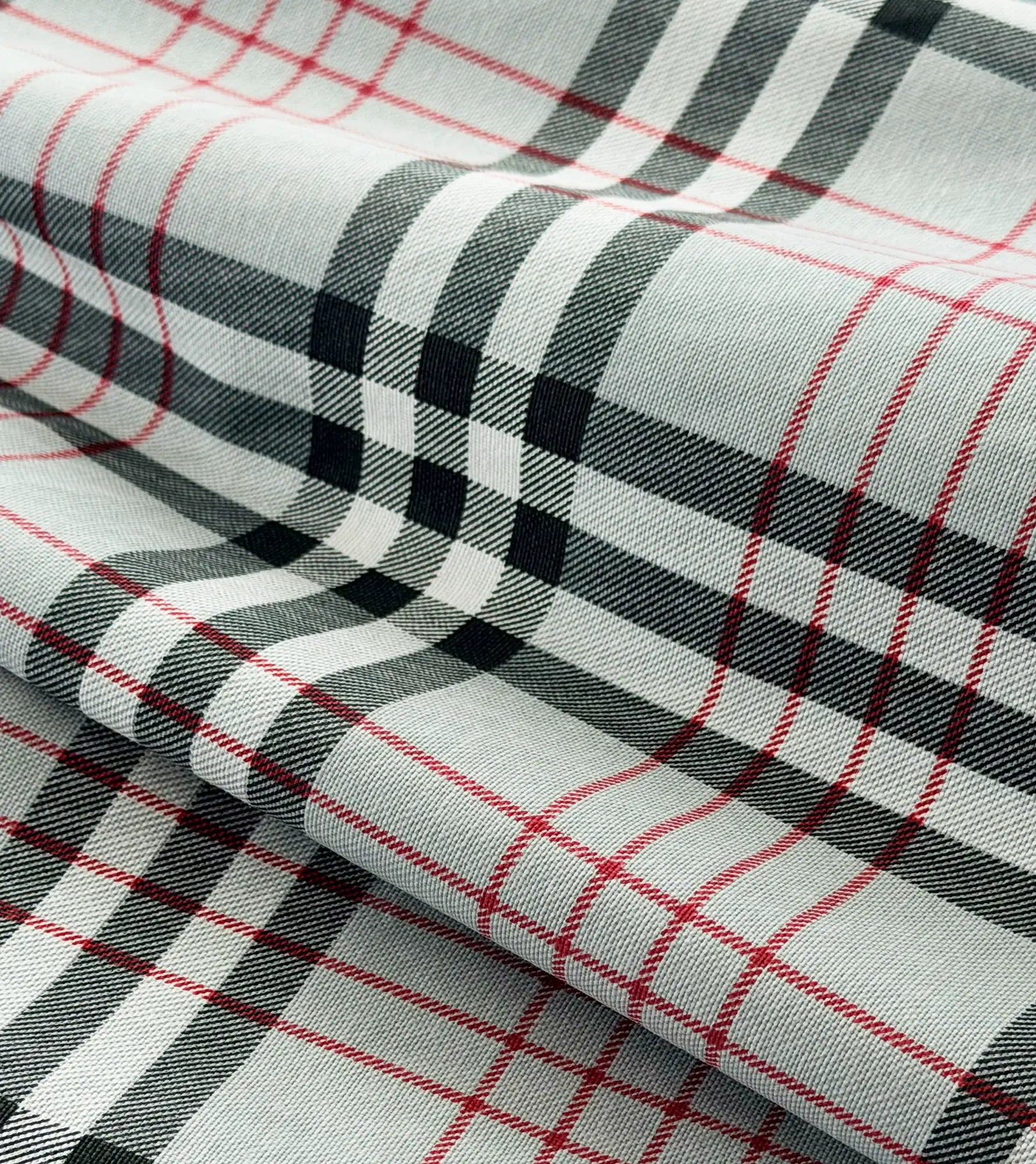 Close-up of plaid fabric with red, black, and white lines on a light gray background.