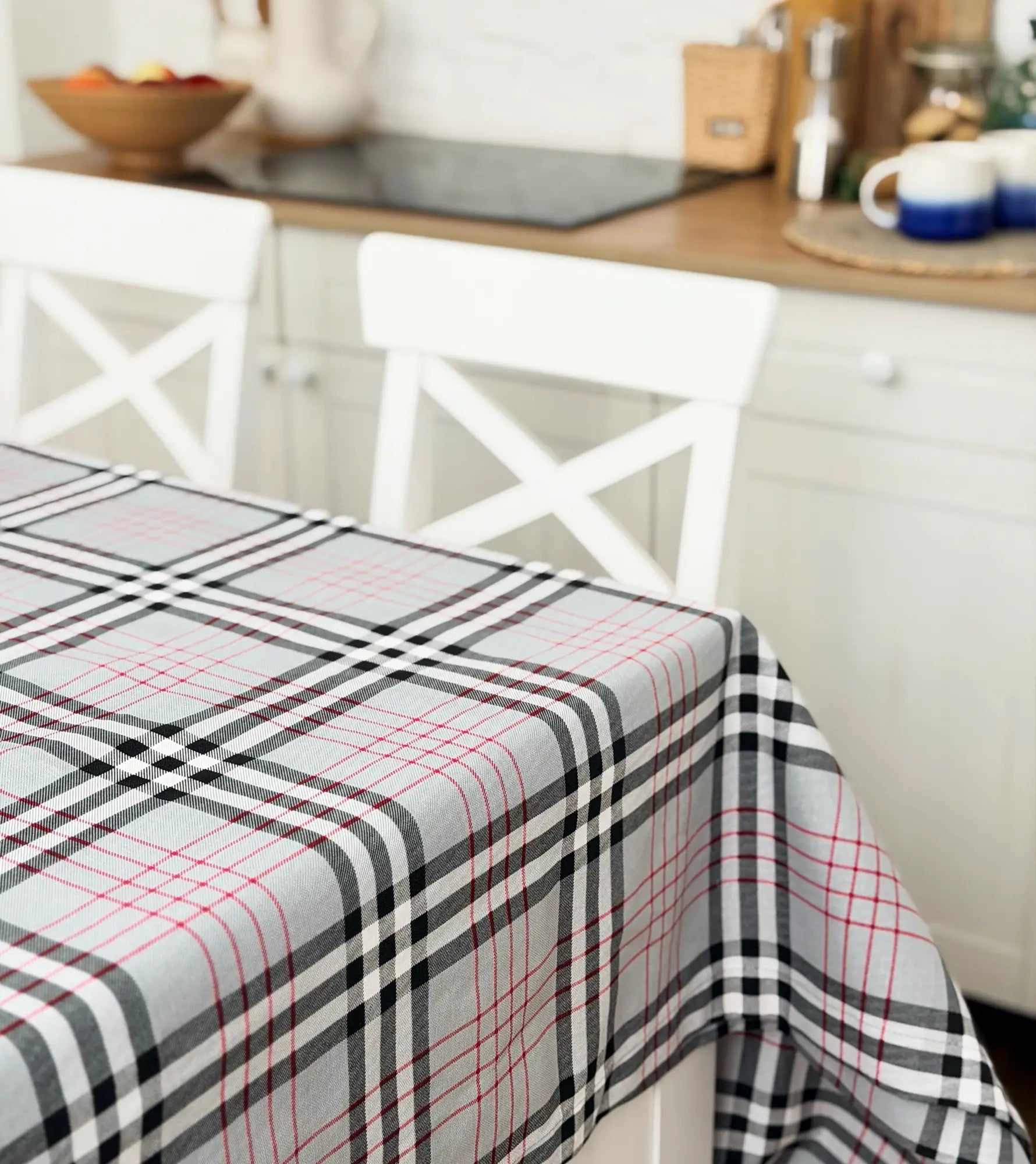 Plaid tablecloth on a kitchen table with white chairs and a blurred background