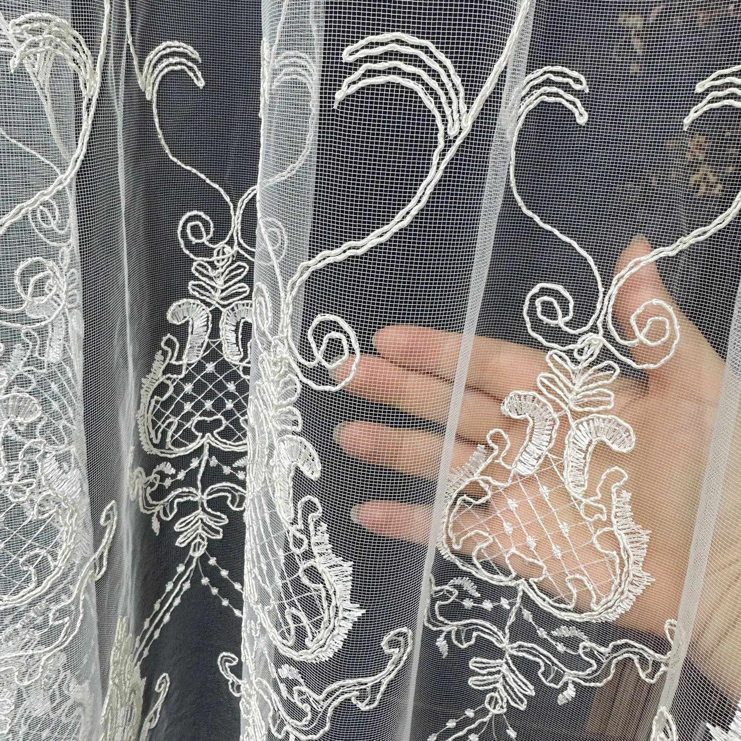 Close-up of white lace fabric with intricate patterns held by a hand against a dark background.