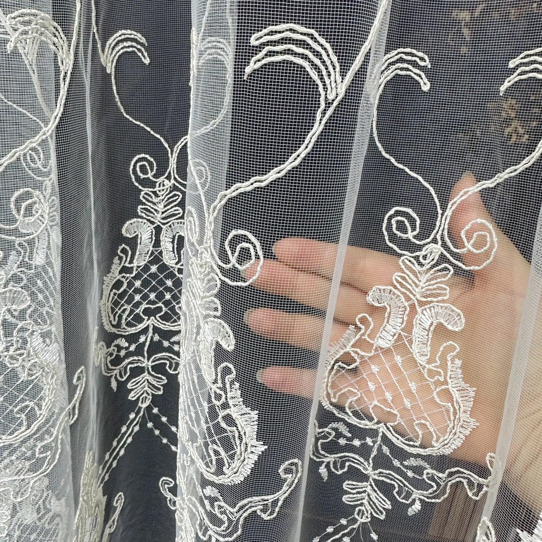 Close-up of white lace fabric with intricate patterns held by a hand against a dark background.