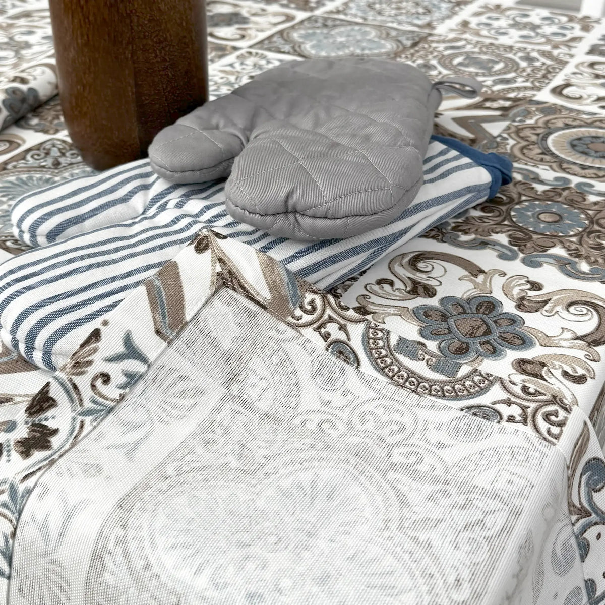Gray oven mitt and striped towel on a patterned tablecloth