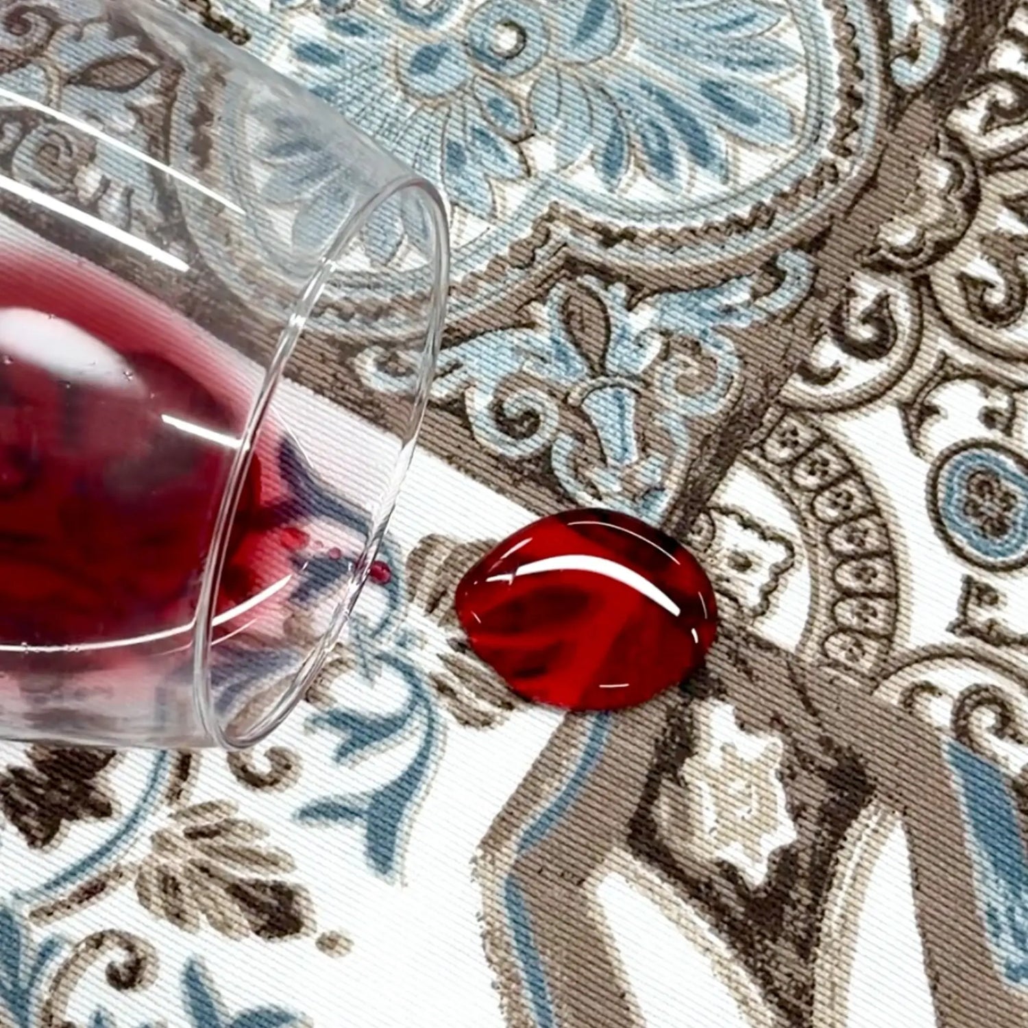 Glass of red wine on a decorative tablecloth with a close-up of a red gemstone.