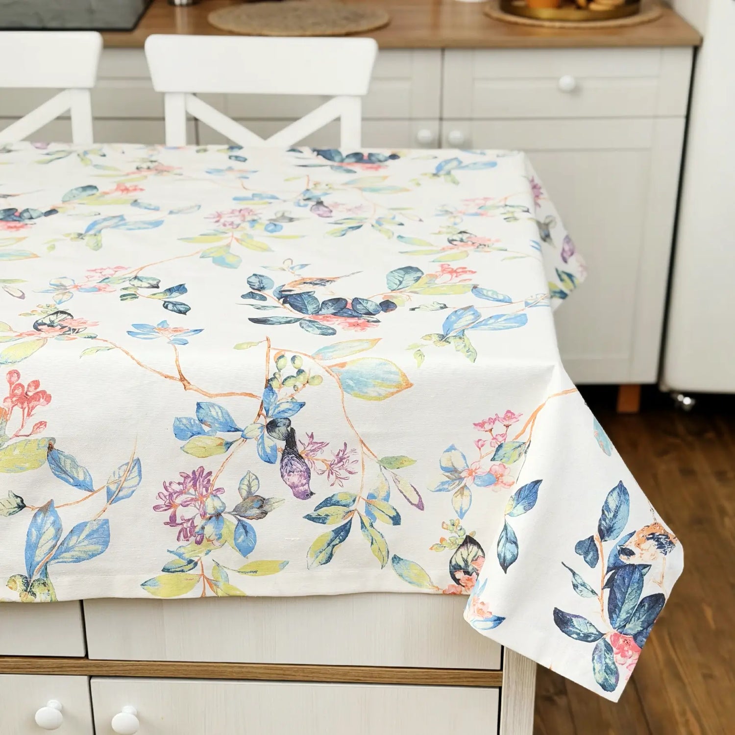 Floral patterned tablecloth on a kitchen table with white chairs.